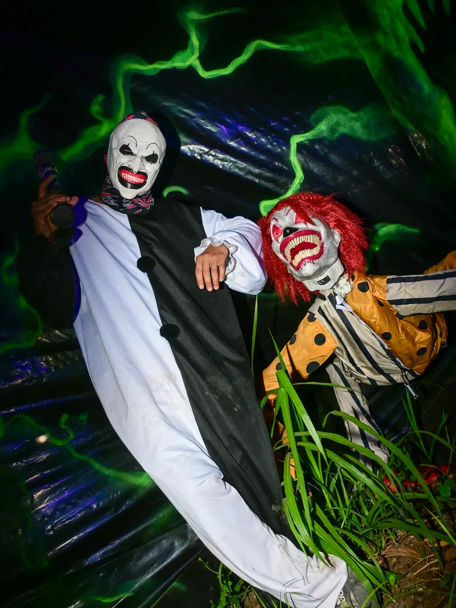 Two clowns in white and orange costumes posing against a green-lit backdrop on the trail